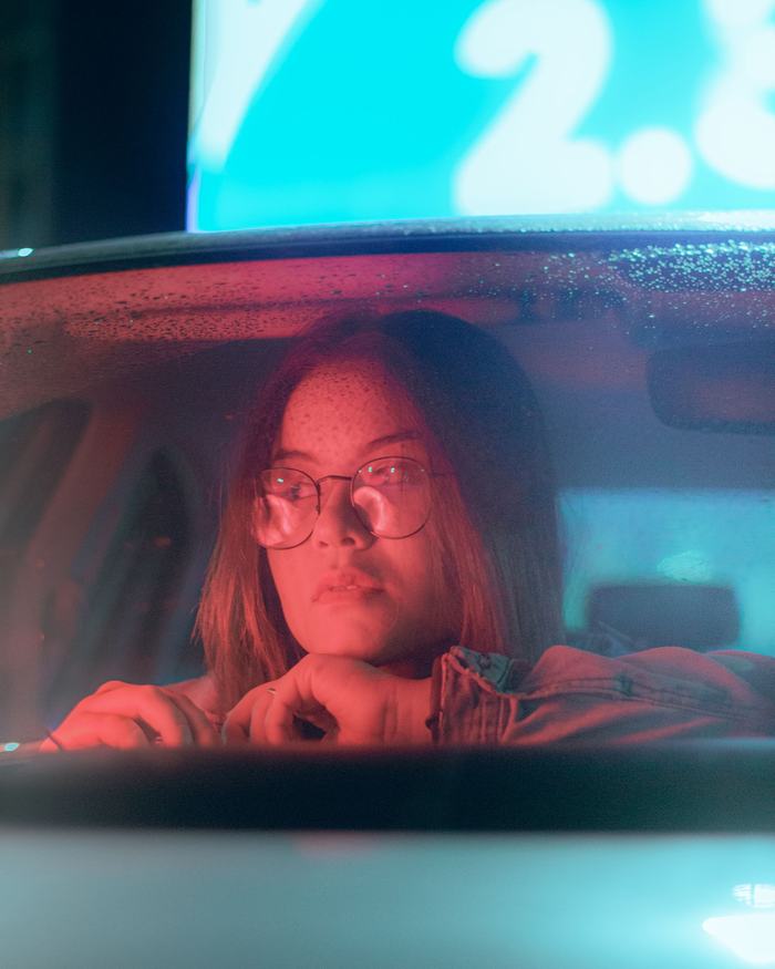 A passenger in the back seat of a car at night, city lights soft beyond the window