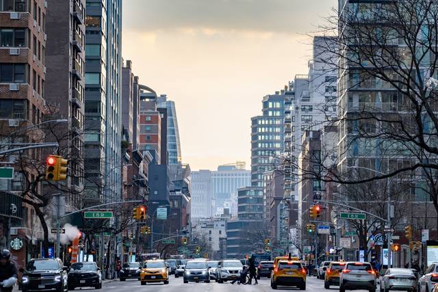 A New York City avenue at dusk, with the skyline above street traffic